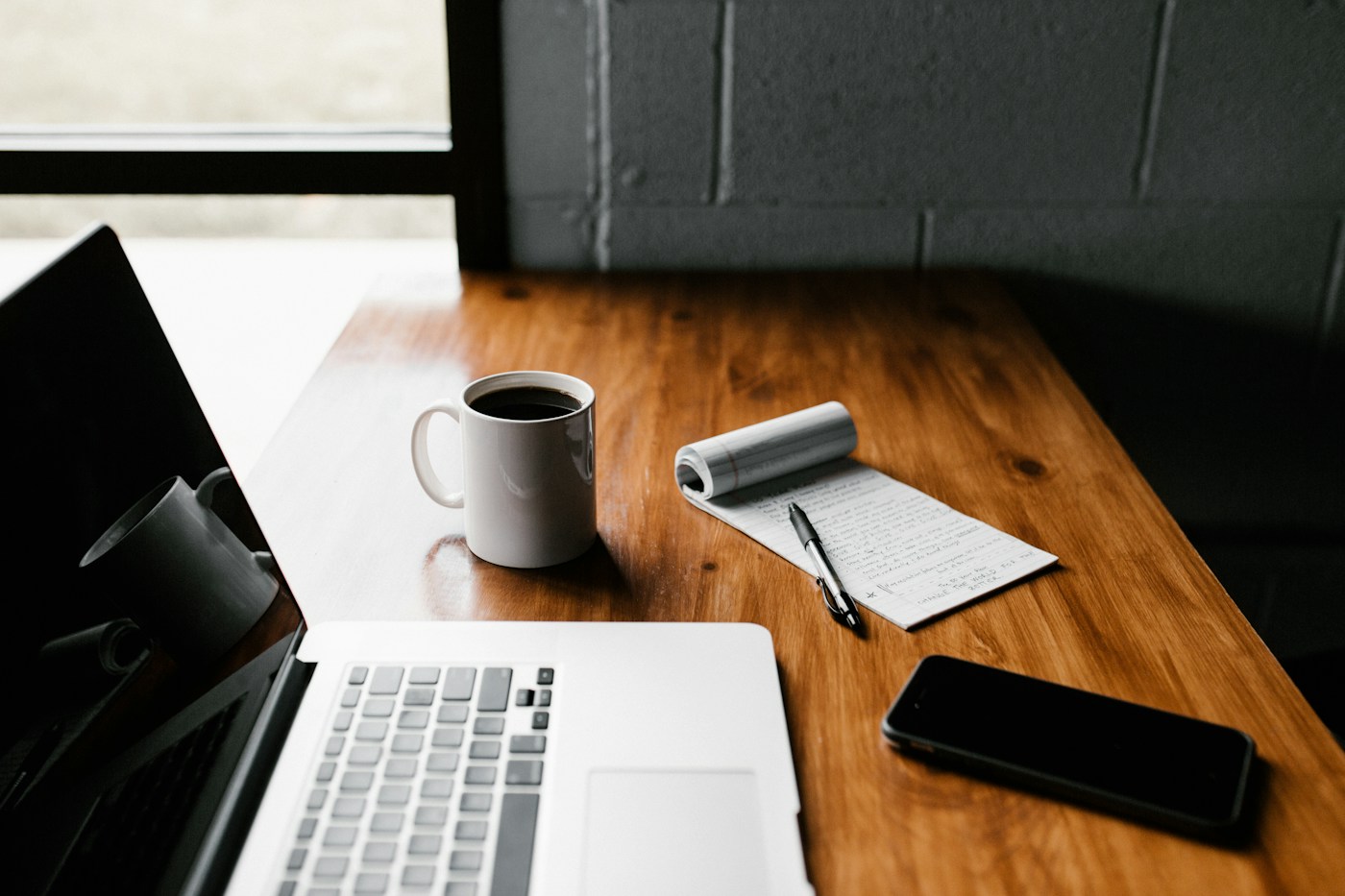 Una scrivania con un computer, un quaderno e una tazza di caffè